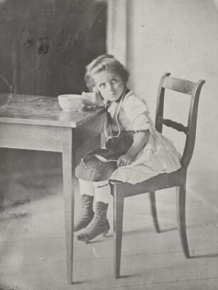 Kleines Mädchen auf einem Stuhl am Tisch