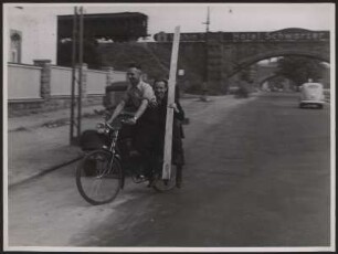 Unfallverhütung. Zwei junge Männer fahren mit einem langen Brett Fahrrad, was sehr gefährlich für den Verkehr ist