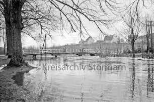 Beste: Kurpark: Hochwasser: Fußgängerbrücke: darauf Frau mit Kind und zwei Jungen: links und rechts Böschung mit Bäumen: hinten rechts Wohnblocks und Wohnhäuser am Meisenweg