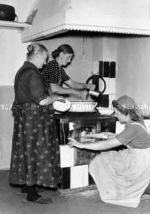 Arbeitsmaid des Reichsarbeitsdienstes beim Feuern des Herdes in einem Bauernhaus (Außendienst)