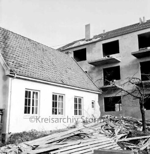 Polizeiwache: Mühlenstraße: links halb abgebrochener Anbau: rechts hinten mehrgeschossiges Wohn- und Geschäftshaus im Rohbau: vorn rechts Baum: daneben Bretterhaufen