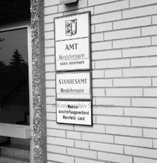 Amtshaus Am Schiefen Kamp: Wand neben Eingang mit Schild der Amtsverwaltung: Klebestreifen mit neuem Namen