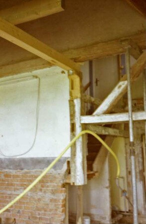 Beimoorweg (47): Fachwerkhaus mit Reetdach: bei Renovierung: Innenansicht: links Innenmauer, rechts Gefache Innenwand ohne Ausmauerung, Metallstütze: hinten Teil von Holztreppe, oben Tür