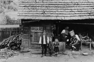Drei Frauen und ein alter Mann mit zwei Kindern vor einem Holzhaus (im Kreis Maramures ?)