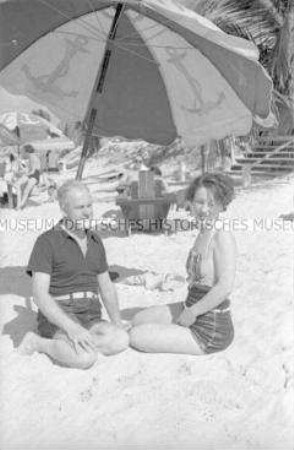 Zwei Touristen am Strand unter einem Sonnenschirm sitzend