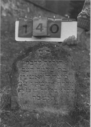 Grabstein 140 (Index: 100008983) Zustand: linker Rand abgebröckelt, unten stark verwittert Maße HxBxT: 45x43x6 cm Besonderheit: Kindergrab?: Grabstein 140