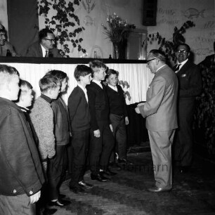 Kreisfußballverband Stormarn: Verbandstag: Reinfeld: Festsaal des "Hotel Stadt Hamburg": Ehrung der Meister: Vorsitzender Erwin Gesche bei Ehrung einer Gruppe von Jungen: dahinter Verbandsleitung auf Podium: Grün- und Blumenschmuck, rechts hinten Tür, 22. Mai 1965