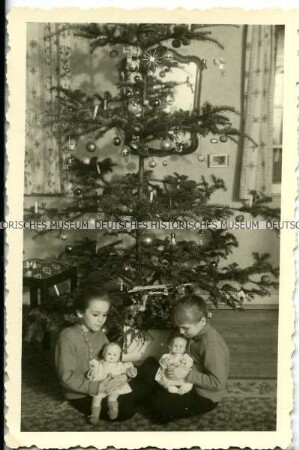 Zwei Mädchen mit Puppen unter dem Weihnachtsbaum