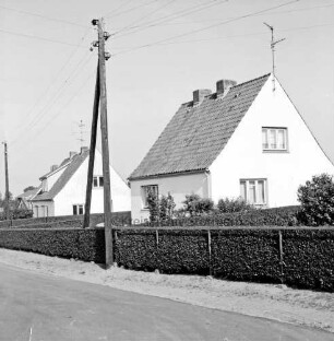 Wiesenweg: Neubausiedlung: Einfamilienhäuser mit Vorgärten, Hecken und Zäunen: vorn Straße: links Strommasten