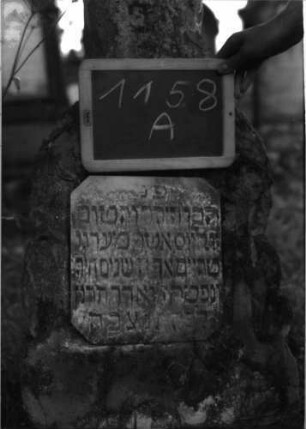Grabstein 1158 (Index: 100104280) Material: Sandstein, Tafel aus Marmor Zustand: angewittert Maße HxBxT: 118x40x22 cm Beschreibung: aufgesockelte Stele in Baumstumpf-Form, Basis felsartig gearbeitet, darin eingelassene rechteckige Schrifttafel mit abgeflachten Ecken Symbolik: Baumstumpf Besonderheit: Kind: Grabstein 1158A