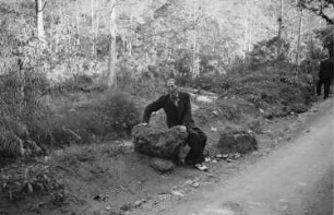 Reisefotos. Tourist, an einer Urwaldstraße auf einem Stein sitzend (vielleicht in Mexiko)