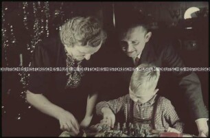 Junge, Mann und Frau mit Kriegsspielzeug vor dem Weihnachtsbaum