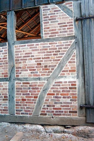 Dorfplatz (2): Fachwerkscheune: Sanierung: Giebelseite, Detailaufnahme: Schwellbalken auf Feldsteinfundament, Gefache mit neuer Ausmauerung, Fensteröffnung, rechts Scheunentor [angeschnitten], oben Blechverkleidung: 8. August 1994