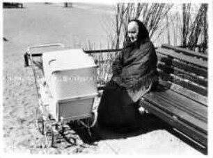 Alte Frau mit Kinderwagen auf einer Parkbank