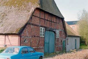 Hauptstraße (7): traufständige Fachwerkkate mit Reetdach: Giebelseite Wirtschaftstrakt mit Scheunentor, Stalltür: rechts Stallquerbau: davor Pkw: im HIntergrund rechts Wohnhaus