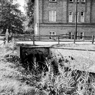 Hoherdammer Mühle: Rentnerwohnheim der Gemeinde: Durchlauf der Norderbeste: darüber Weg mit Geländer: hinten links Bäume: vorn Schilf