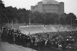 Blick in die Radrennbahn in Reick während der Wahlveranstaltung der KPD, an der Bande die Losung:"Kommunismus ist der einzige Ausweg!", im Hintergrund das Gasometer Reick