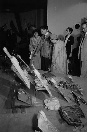 Mehrere Personen betrachten die auf einem Stand auf der Leipziger Herbstmesse 1955 ausgestellte Herrenoberbekleidung