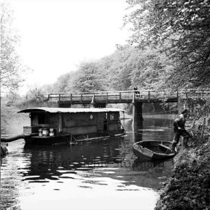 Trave: Entschlammungsarbeiten: Schwimmbagger mit Saugrohren: vorn rechts Arbeiter beim verlassen des Ruderbootes: hinten Friedensbrücke: darauf Zuschauer: im Hintergrund Wald