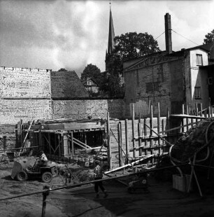 Firma Carl Hoffmann: Hindenburgstraße: Elektrohandel: Neubau: Fundament: Blick in Baugrube mit Baumaschine, Arbeitern und Baumaterial: hinten weitere Gebäudeteile: hinten Mitte Turm der Peter-Paul-Kirche zwischen Bäumen