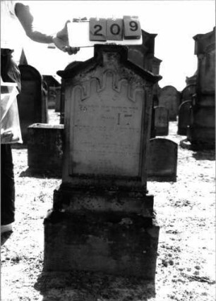 Grabstein 209 (Index: 99797665) Material: Sandstein, weiß Zustand: leicht verwittert Maße HxBxT: 108x47x19 cm Beschreibung: Stele, giebelartiger Abschluß rechteckig erhöht, getreppter Sockel Symbolik: Rundbogenfries: Grabstein 209