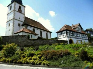 Ansicht von Nordosten mit Kirche über Kirchhofmauer (Wehrgang mit Brüstung abgetragen) sowie (verändertem ) Torbau in Übersicht