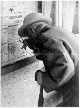 Alter Mann liest mit einer Lupe den Bahnfahrplan (Altersgruppe bis 14)