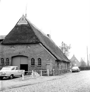 Schlamersdorf: Dorfstraße mit Kopfsteinpflaster: links Bauernhaus mit Reetdach: links daneben Geländer und Pkw: hinten rechts Pkw: dahinter Wohnhaus