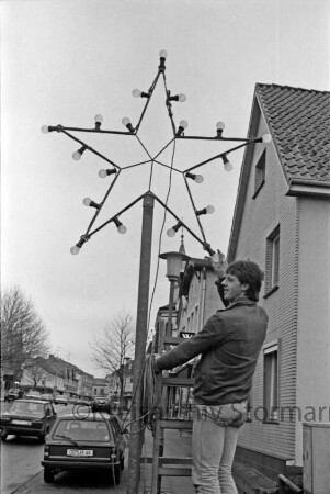 Advent: Paul-von-Schoenaich-Straße: Mann bei Installation der Adventsbeleuchtung: hinten rechts Wohn- und Geschäftshäuser: links Pkw