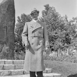 Mann in Hut und Mantel im Park vor einem Denkmal