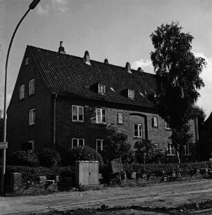 Hebbelstraße: Ausbau: vorn unbefestigte Straße, Stapel mit Gehwegplatten und Stromverteilerkasten: dahinter Wohnhäuser der Gemeinnützigen Baugenossenschaft Bad Oldesloe mit Vorgärten