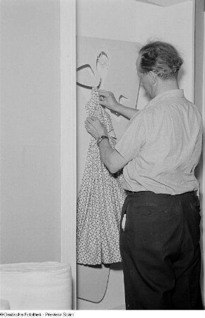 Ein Mann beim Dekorieren einer Vitrine der Leipziger Herbstmesse 1954 mit einer Textilie