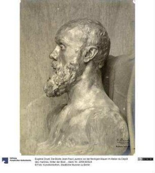Die Büste Jean-Paul Laurens vor der fleckigen Mauer im Atelier du Dépôt des marbres, hinter der Büste eine Stoffdraperie