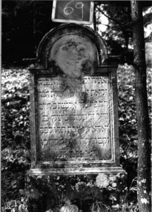 Grabstein 69 (Index: 100090677) Material: Sandstein Zustand: abgeblättert mit Textverlust Maße HxBxT: 118x53x14 cm Beschreibung: Stele, profiliert. Sockel, eingezog. Rundbogenabschl. m. Verdach. , Schrift eingetieft: Grabstein 69