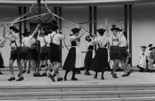 Menschen in Tracht tanzen um einen Maibaum