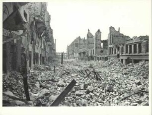 Blick auf eine von Trümmern verschüttete Straße, seitlich Reste der zerstörten Häuser
