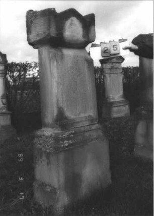 Grabstein 25 (Index: 99808564) Material: Sandstein Zustand: stark verwittert, mit Zement ausgebessert, Schrifttafel fehlt Maße HxBxT: 161x60x32 cm Beschreibung: Stele, profilierter Sockel, Giebel mit Eckakroteren, eingesetzte Schrifttafel (fehlt): Grabstein 25