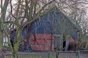 Dorfplatz (2): Fachwerkscheune: Giebelseite mit Scheunentor, Traufseite: oberer Gebäudeteil mit Verkleidung: Bäume, Zaun