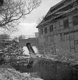 Drahtmühle: Restaurierung: vorn Mühlenbach: links Brücke mit Wehr: oben rechts Stapel mit Brettern: links Baum: Winter