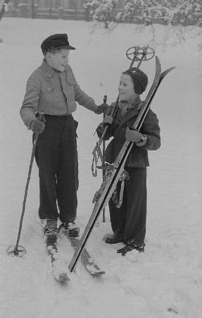 Kinder beim Ski- und Schlittenfahren, zwei Jungen mit Skiern nach der Abfahrt
