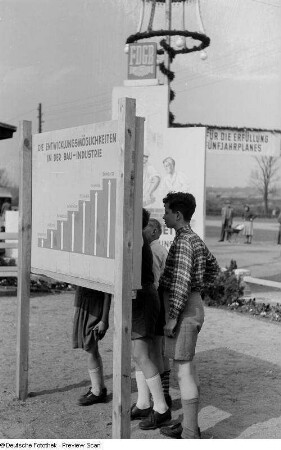 Kinder vor einer Informationstafel über die beruflichen Entwicklungsmöglichkeiten in der DDR-Bauindustrie