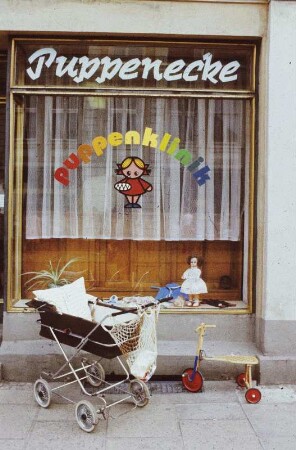 DDR. Abgestellter Kinderwagen und Dreirad vor dem Schaufenster "Puppenecke" (Puppenklinik)