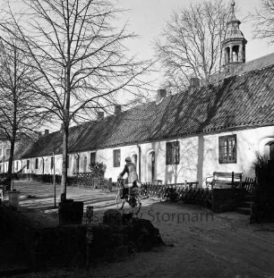 Gottesbuden: südliche Reihe: Jägerzaun, Ruhebank: davor Weg, Frau auf Fahrrad: rechts dahinter Dachreiter von Schlosskirche