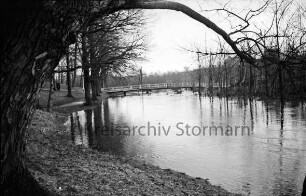 Beste: Kurpark: Hochwasser: hinten Mitte Fußgängerbrücke: darauf zwei Jungen: hinten links Personen im Park: hinten rechts Wohnblocks am Meisenweg hinter Bäumen