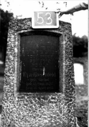Grabstein 53 (Index: 100110260) Material: Granit mit schwarzer Marmorplatte Zustand: gut Maße HxBxT: 122x67x33 cm Beschreibung: grob stelenhaft behauener Stein, Segmentbogenabschluß, Schriftplatte: Grabstein 53