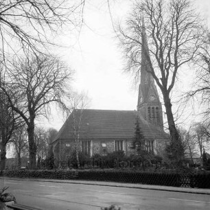 Friedenskirche, davor Kastanienbäume auf dem Kirchengelände, vorne die Hauptstraße
