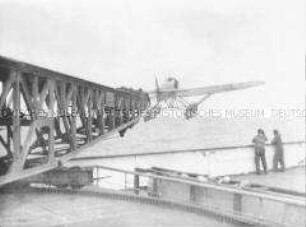 Zwei Personen an der Reling beobachten den Start des Katapultflugzeugs HE 12 D-1717 vom Hochseepassagierdampfer "Bremen"