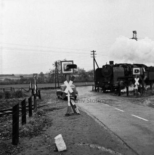 Siebenbäumen (Kreis Herzogtum Lauenburg): Bahnstrecke zwischen Bad Oldesloe und Ratzeburg: Bahnübergang der Landstraße zwischen Bad Oldesloe und Ratzeburg: Filmaufnahmen der Reginald Puhl Filmproduktion aus Hamburg-Wandsbek zum Dokumentarfilm "Todesfallen": nachgestellter Bahnunfall einer Dampflokomotive mit einem Pkw: in der Mitte Bahnübergang mit Signalanlagen: darauf Pkw: rechts fahrende Dampflokomotive: dahinter Strommasten: vorn links Zaunpfähle: im Hintergrund Wiesen und Bäume