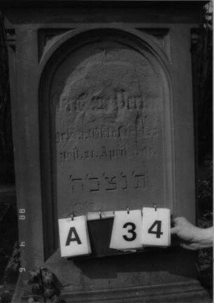 Grabstein 34 (Index: 99792843) Material: Sandstein Zustand: stark verwittert mit Textverlust Maße HxBxT: 156x65x36 cm Beschreibung: Stele, Sockel profiliert, eingezogener Rundbogenabschluß mit Verdachung, Schriftfeld eingetieft mit Rundbogenabschluß: Grabstein 34A