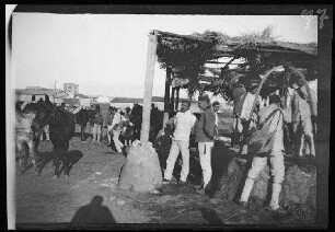 Nador (Marokko): Offiziere, Soldaten und Pferde [des spanischen 8. Kavallerie-Regiments "Lusitania"] an einer mit Stroh überdachten, gemauerten und mit einem Metallbügel über dem Brunnenloch ausgestatteten Wasserstelle ("Tränken der 3. und 4. Eskadron am Brunnen")